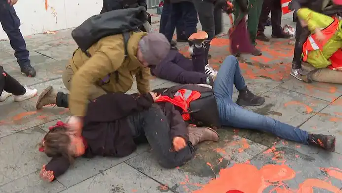 Ein Zivilpolizist in Berlin schmiert Klimaaktivist mit einem Klimaaktivisten mit einem Pinsel Farbe ins Gesicht